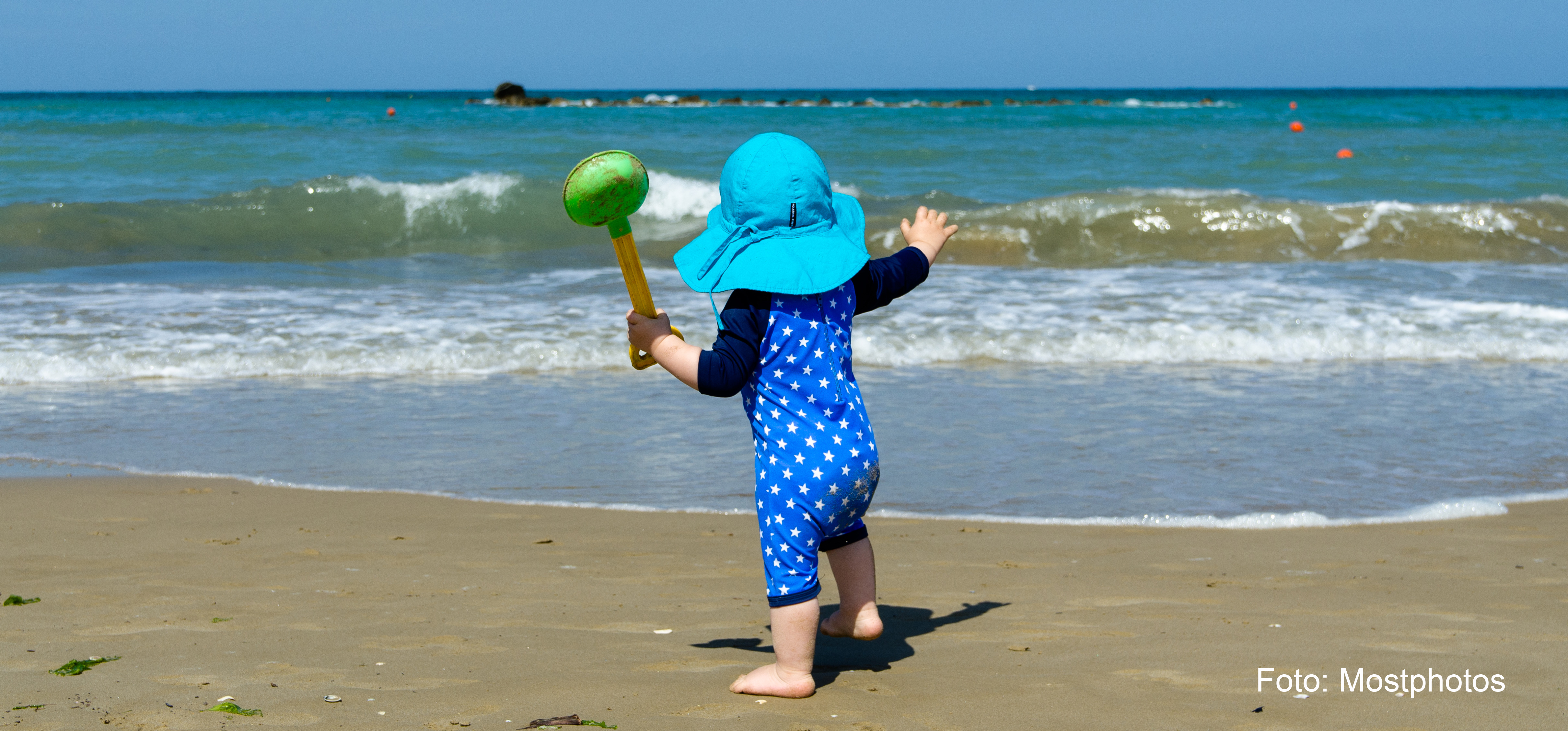 Bilden visar ett litet barn som står på stranden och spanar ut över vattnet.