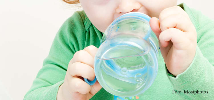 Ett litet barn dricker vatten ur en mugg.